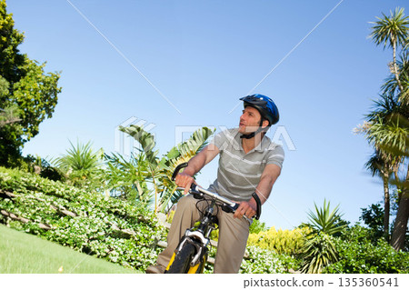 Man in his thirties riding yellow bike across manicured lawn wearing blue helmet, copy space Man in his thirties riding yellow bike across manicured lawn wearing blue helmet, copy space 135360541
