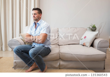 Man sitting barefoot on left side of couch in living room with potted plant, copy space Man sitting barefoot on left side of couch in living room with potted plant, copy space 135360543