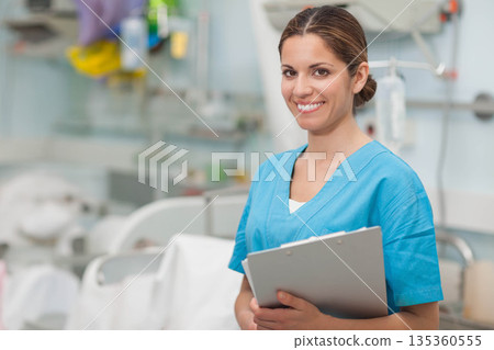 Female nurse holding clipboard while standing in hospital ward with IV stand and beds, copy space Female nurse holding clipboard while standing in hospital ward with IV stand and beds, copy space 135360555