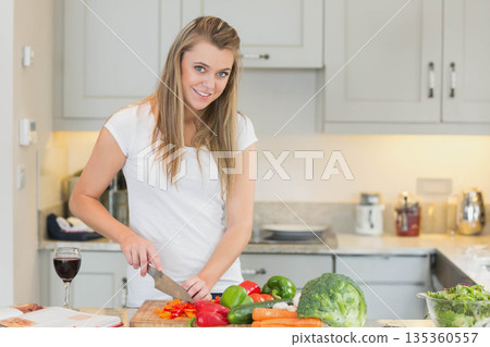 Woman slicing red bell pepper on cutting board at kitchen island between cookbook and wine glass 135360557