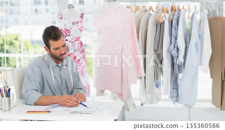 Hispanic man sketching fashion designs with pencil at studio with sewing machine and dress form 135360566