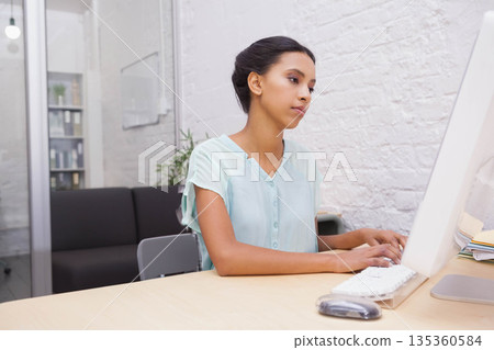 African American woman typing on desktop computer at office desk with keyboard mouse and plant African American woman typing on desktop computer at office desk with keyboard mouse and plant 135360584