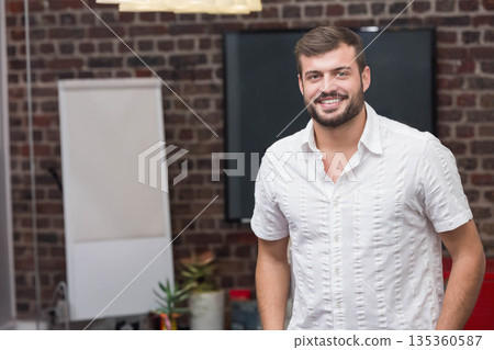 Man in late twenties standing in modern coworking area beside flip chart easel and pendant light Man in late twenties standing in modern coworking area beside flip chart easel and pendant light 135360587