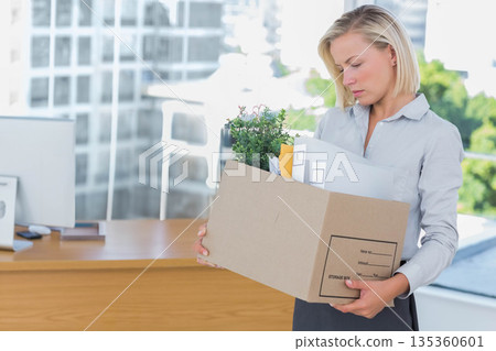 Female office worker packing plant and files into cardboard box beside desk at office, copy space Female office worker packing plant and files into cardboard box beside desk at office, copy space 135360601