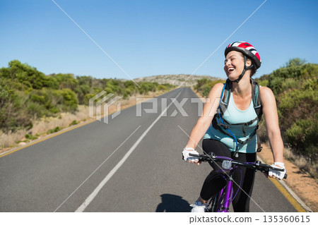 Female cyclist riding purple bike on road, slowing with helmet gloves hydration pack, copy space 135360615