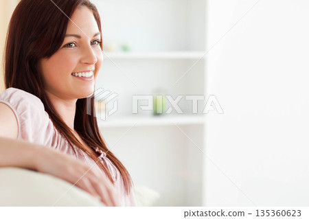 Woman with long brown hair sitting on couch leaning back by white shelving unit, copy space Woman with long brown hair sitting on couch leaning back by white shelving unit, copy space 135360623