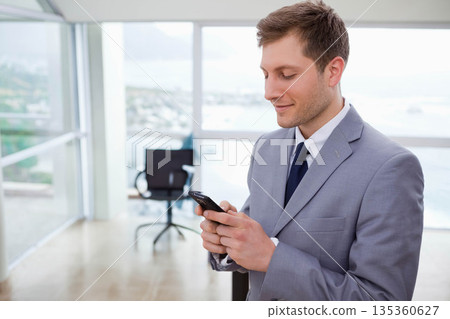 Adult man holding smartphone tapping screen near panoramic windows in office, copy space 135360627