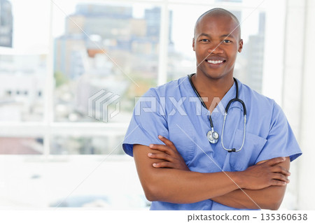 African American male doctor standing in clinic wearing scrubs with stethoscope smiling confidently 135360638