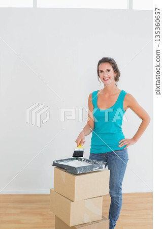 Woman in tank top painting wall at home using paintbrush above tray on boxes, copy space Woman in tank top painting wall at home using paintbrush above tray on boxes, copy space 135360657