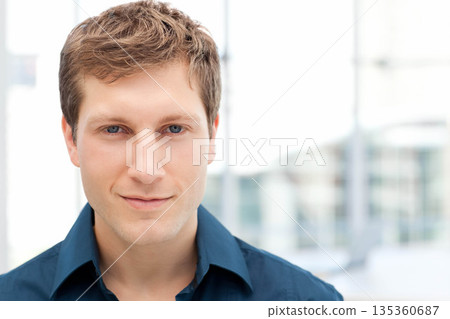 Businessman wearing navy-blue collared shirt smiling behind glass panels in modern office 135360687