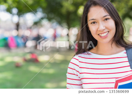 Asian woman student standing on quad carrying red notebook, blue binder and backpack, copy space Asian woman student standing on quad carrying red notebook, blue binder and backpack, copy space 135360699