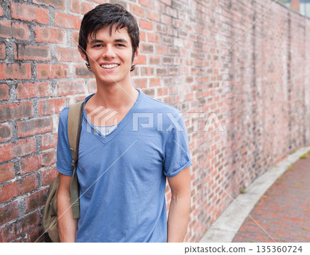Male leaning against red brick wall on walkway wearing green canvas backpack, copy space Male leaning against red brick wall on walkway wearing green canvas backpack, copy space 135360724