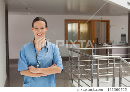 female nurse standing in hospital corridor wearing scrubs and stethoscope by railing, copy space female nurse standing in hospital corridor wearing scrubs and stethoscope by railing, copy space 135360725