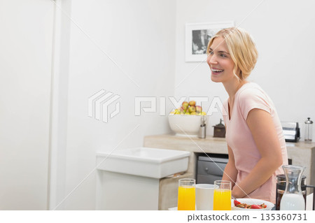 Female leaning on kitchen counter at home, holding clear pitcher by glasses of juice, copy space Female leaning on kitchen counter at home, holding clear pitcher by glasses of juice, copy space 135360731