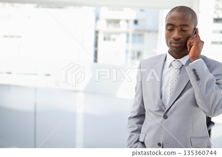 African American man in gray suit talking on smartphone by window in office, copy space 135360744