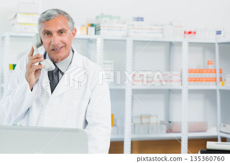 Senior male pharmacist using telephone handset at pharmacy counter with stocked shelves, copy space Senior male pharmacist using telephone handset at pharmacy counter with stocked shelves, copy space 135360760
