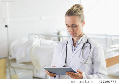 Female doctor in lab coat holding stethoscope and tablet reviewing data at bedside, copy space Female doctor in lab coat holding stethoscope and tablet reviewing data at bedside, copy space 135360771