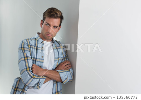 Male leaning with arms folded and gazing to his right in minimalist corner wearing plaid shirt Male leaning with arms folded and gazing to his right in minimalist corner wearing plaid shirt 135360772