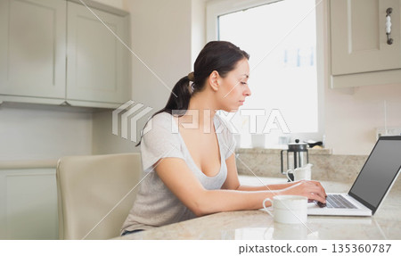 Woman typing on laptop at marble kitchen island with coffee mug and press, copy space Woman typing on laptop at marble kitchen island with coffee mug and press, copy space 135360787