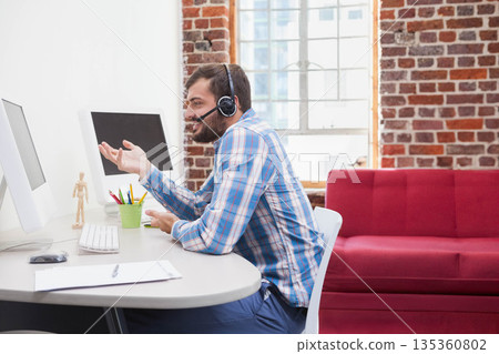 African American man gesturing while speaking in office at desk with dual monitors and headset 135360802