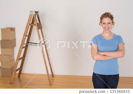 Woman standing near wooden ladder and cardboard moving boxes in empty room, copy space 135360835