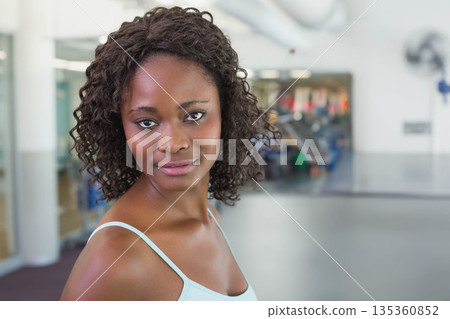 African American woman standing in gym wearing light blue tank top beside cardio machines African American woman standing in gym wearing light blue tank top beside cardio machines 135360852