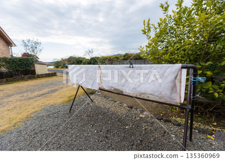 A landscape photo of futon covers drying in the garden. The futon is dried on a rack on gravel. 135360969