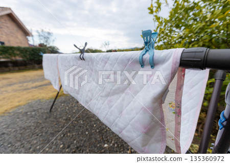 A landscape photo of futon covers drying in the garden. The futon is dried on a rack on gravel. 135360972