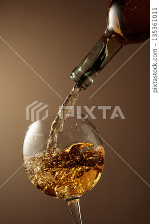 Pouring white wine from a bottle into a glass. Pouring white wine from a bottle into a glass. 135361011