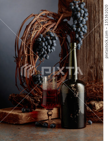 An antique bottle of port wine against the backdrop of an old weathered board, dried vine, and blue grapes. An antique bottle of port wine against the backdrop of an old weathered board, dried vine, and blue grapes. 135361020