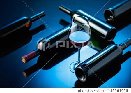Glass and bottles of red wine on a black reflective background. 135361036