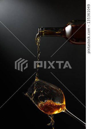 White wine of rich amber color being poured into a glass. 135361049