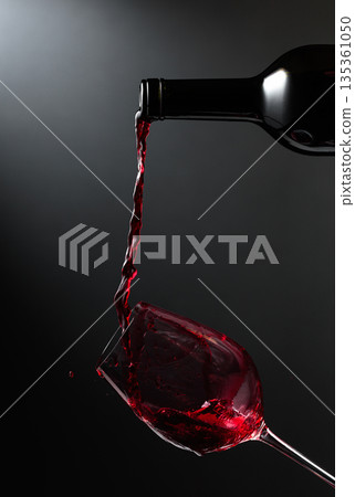 Red wine of rich color being poured from a bottle into a glass. Red wine of rich color being poured from a bottle into a glass. 135361050