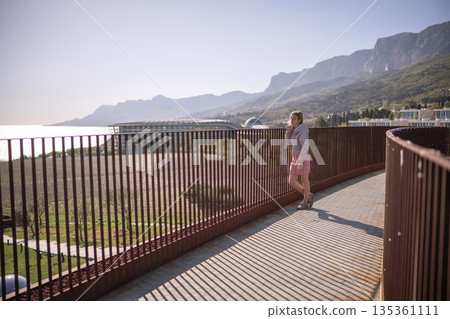 Woman standing on modern balcony railing overlooking sea and majestic mountains travel landscape Woman standing on modern balcony railing overlooking sea and majestic mountains travel landscape 135361111