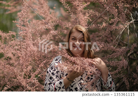 Woman blooming nature portrait smiling in pink tamarix flowers in spring garden 135361115