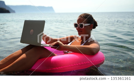 Laptop beach water: Woman works remotely on laptop, floats in tube, seaside, daytime, enjoying leisure Laptop beach water: Woman works remotely on laptop, floats in tube, seaside, daytime, enjoying leisure 135361161