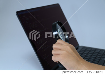 A hand using a magnifying glass to enlarge the cord of a laptop A hand using a magnifying glass to enlarge the cord of a laptop 135361879