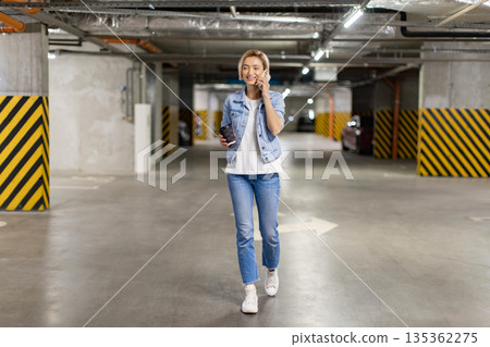 A woman walks through a parking garage while talking on her phone and holding a coffee cup A woman walks through a parking garage while talking on her phone and holding a coffee cup 135362275