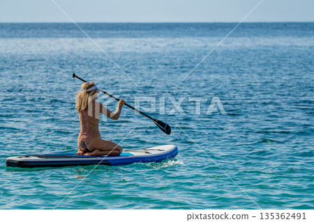 Paddleboarding woman ocean enjoying summer leisure activity on calm sea Paddleboarding woman ocean enjoying summer leisure activity on calm sea 135362491