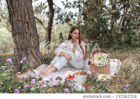 Picnic Flowers Strawberry: Woman eats strawberry in forest picnic during daytime for relaxation. Picnic Flowers Strawberry: Woman eats strawberry in forest picnic during daytime for relaxation. 135362558