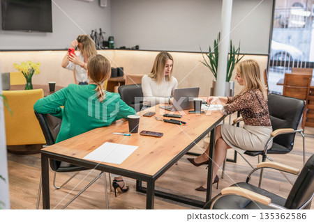 Businesswomen collaboration modern office setting discussing strategy around laptop 135362586