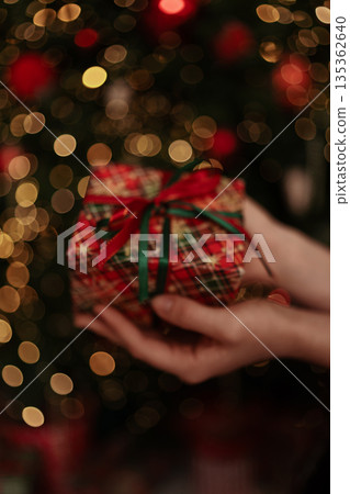 Christmas gift hands holding festive present against warm golden bokeh background Christmas gift hands holding festive present against warm golden bokeh background 135362640