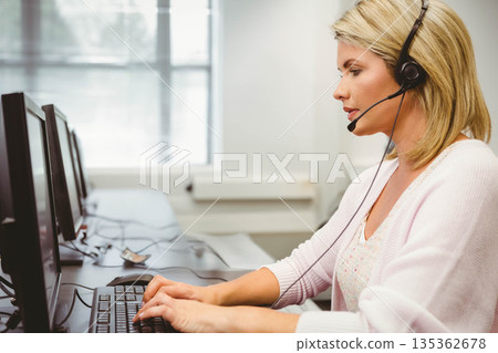 Female call center agent typing on keyboard at office desk with monitors, headset, copy space Female call center agent typing on keyboard at office desk with monitors, headset, copy space 135362678