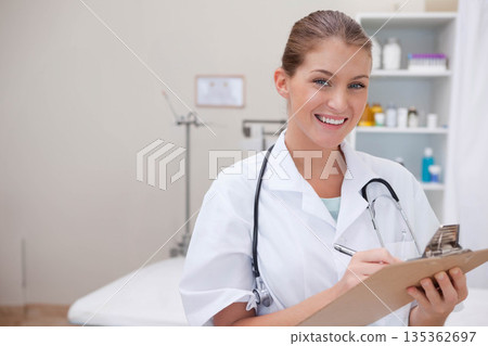 Female medical professional wearing coat holding clipboard and stethoscope in exam room, copy space 135362697