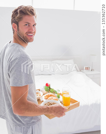 Man standing in bright bedroom holding wooden tray with cereal, croissant and red rose, copy space Man standing in bright bedroom holding wooden tray with cereal, croissant and red rose, copy space 135362710