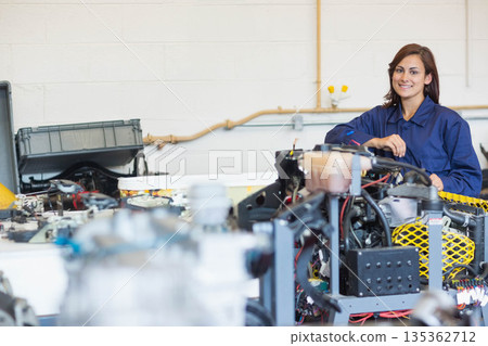 Woman wearing blue coveralls inspecting engine assembly on workbench in workshop, copy space 135362712