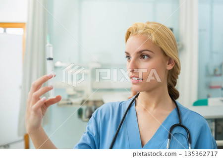 Female medical professional examining green fluid syringe in exam room with stethoscope, copy space Female medical professional examining green fluid syringe in exam room with stethoscope, copy space 135362717