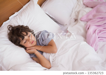 Boy sleeping on side in bed with white bedding, pink blanket and wooden headboard Boy sleeping on side in bed with white bedding, pink blanket and wooden headboard 135362723