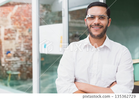 Man wearing white shirt and smart glasses with arms crossed at office showing green chalkboard 135362729