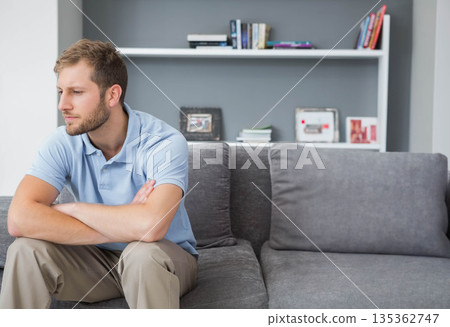 Man sitting arms crossed gazing left on sofa in living room with floating shelf, copy space 135362747
